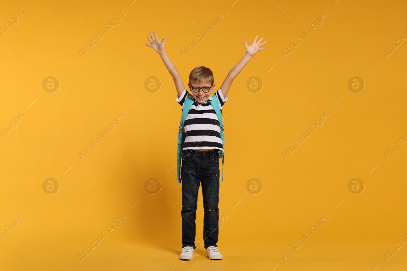 Photo of Emotional schoolboy in glasses with backpack on orange background