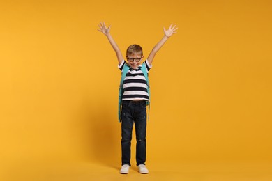 Photo of Emotional schoolboy in glasses with backpack on orange background