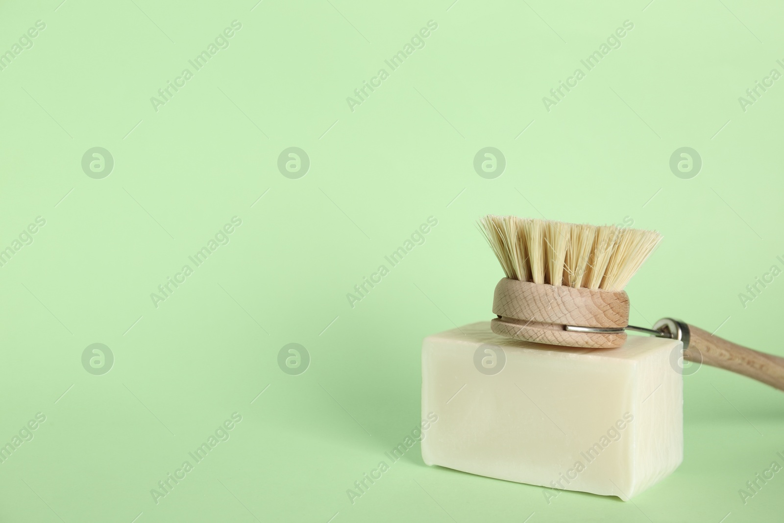 Photo of Cleaning brush and soap bar on green background, space for text. Dish washing supplies