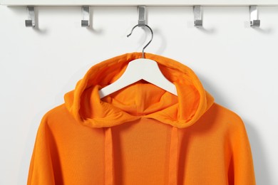 Photo of Hanger with orange hoodie on white wall