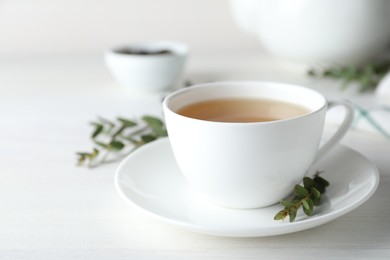 Photo of Cup of green tea and eucalyptus leaves on white table. Space for text
