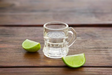 Mexican tequila shot with lime slices on wooden table, closeup. Drink made from agave