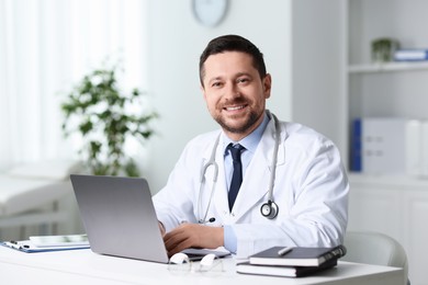 Smiling doctor with laptop at table in clinic. Online consultation