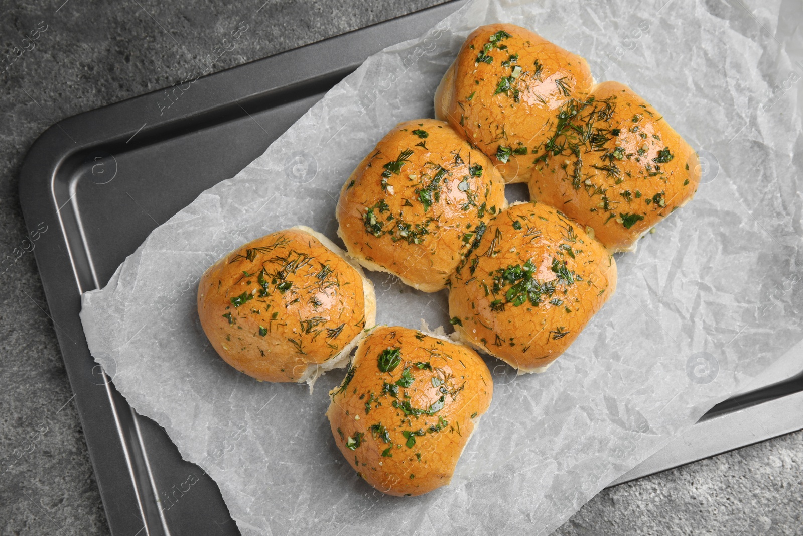 Photo of Traditional pampushka buns with garlic and herbs on baking dish, top view