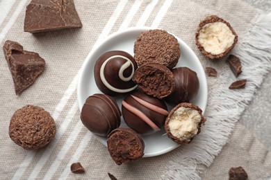 Photo of Many different delicious chocolate truffles on kitchen towel, flat lay