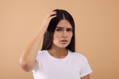 Photo of Emotional woman examining her hair and scalp on beige background