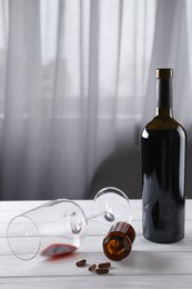 Alcohol and drug addiction. Overturned glass with red wine, bottle and pills on white wooden table