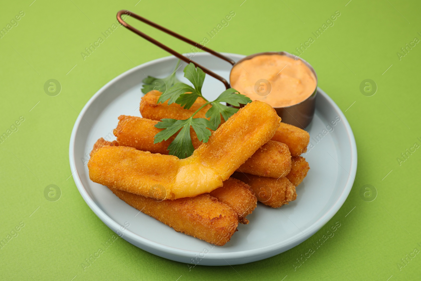 Photo of Tasty fried mozzarella sticks served with sauce and parsley on green background
