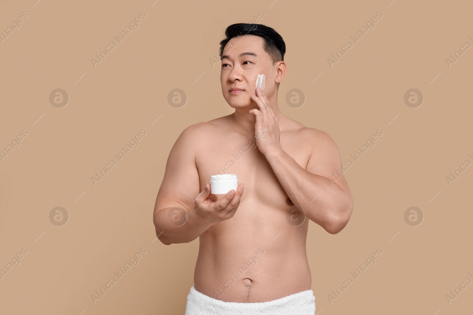 Photo of Handsome man applying cream onto his face on light brown background