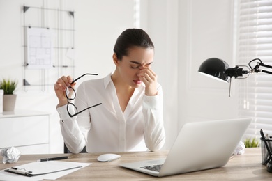 Stressed and tired young woman with headache at workplace