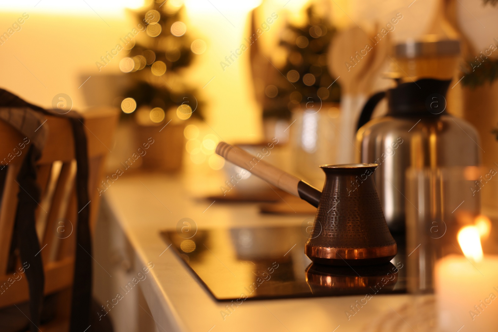 Photo of Beautiful copper coffee pot on cooktop in kitchen against blurred Christmas lights, space for text