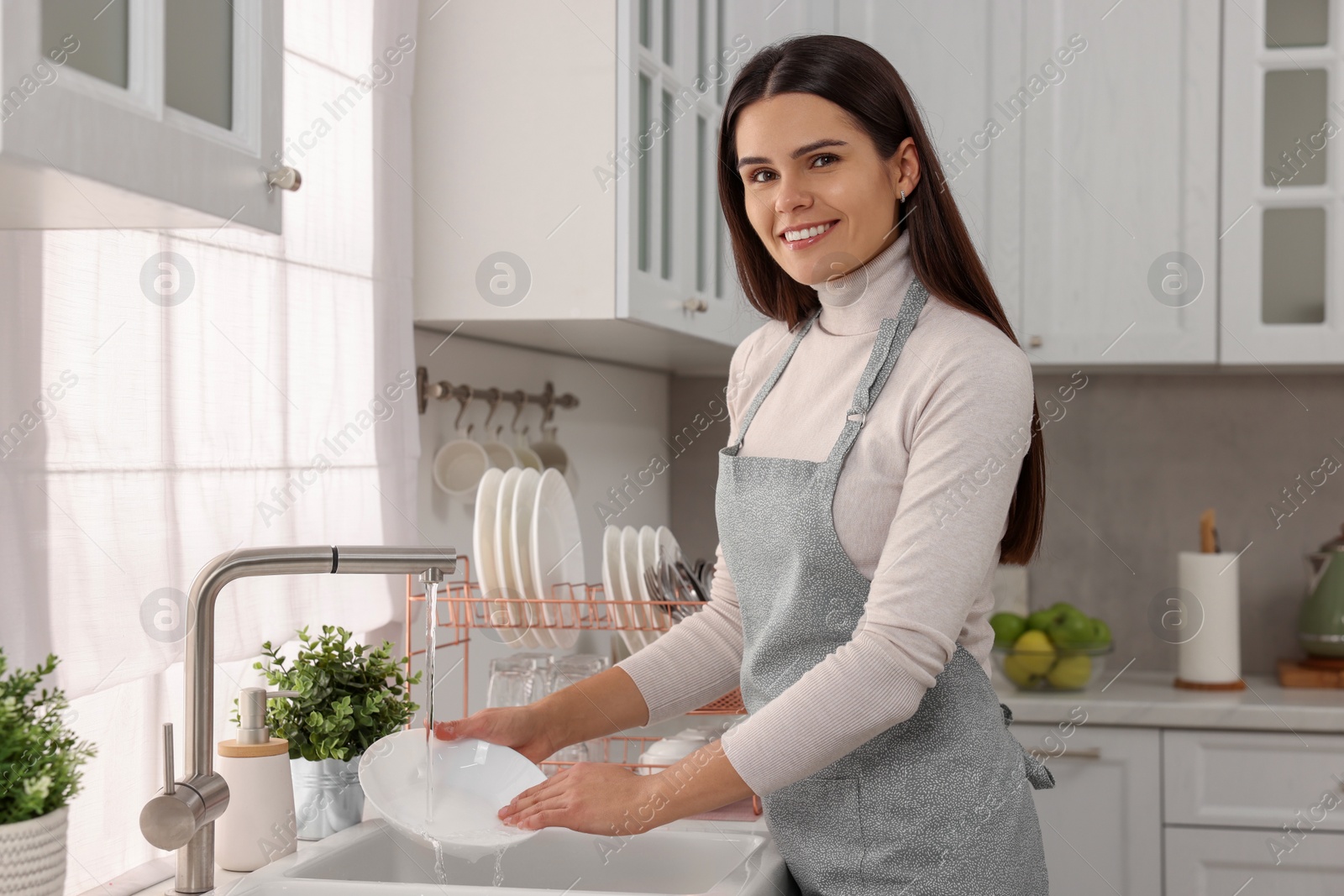 Photo of Happy woman washing bowl at sink in kitchen