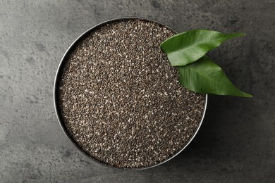 Photo of Bowl with chia seeds and green leaves on grey table, top view
