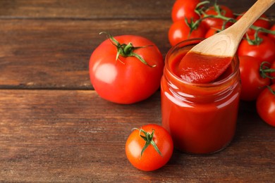 Photo of Taking tasty ketchup with spoon from jar on wooden table, closeup. Space for text