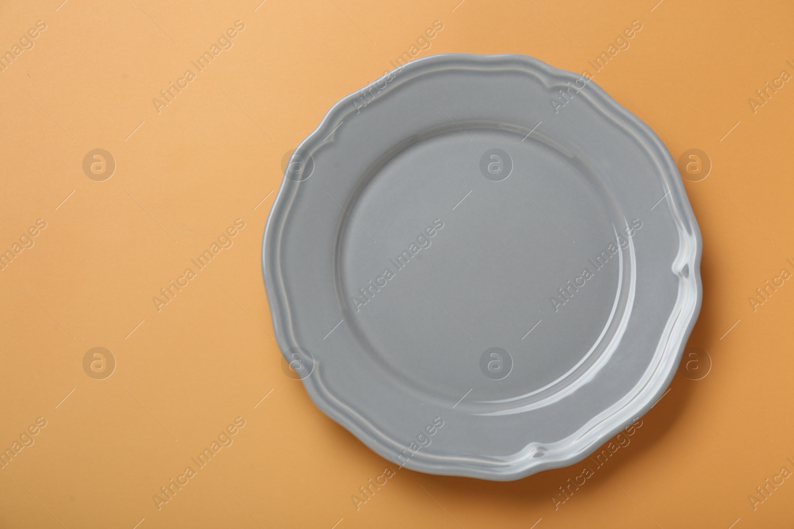 Photo of Empty ceramic plate on pale orange background, top view. Space for text