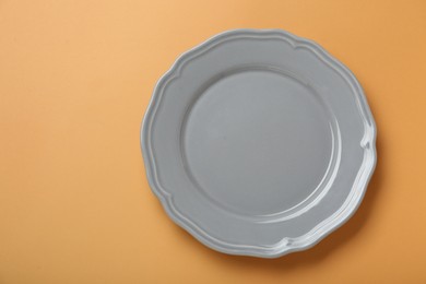 Photo of Empty ceramic plate on pale orange background, top view. Space for text