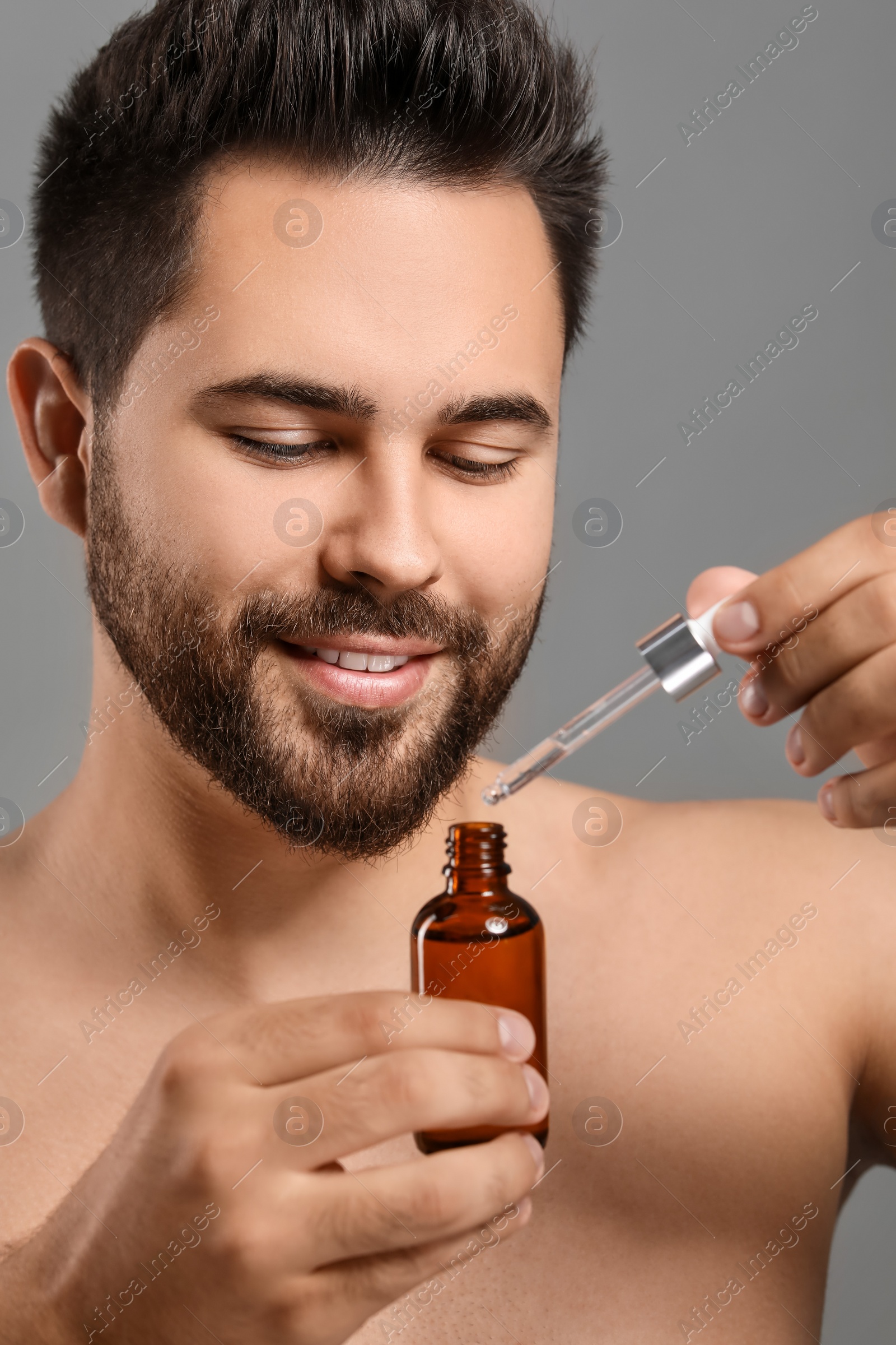 Photo of Handsome man with cosmetic serum in hands on grey background