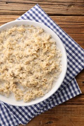 Photo of Tasty boiled oatmeal in bowl on wooden table, top view