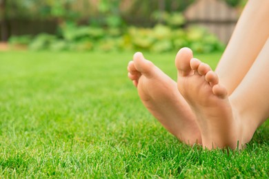 Photo of Woman sitting barefoot on fresh green grass outdoors, closeup. Space for text