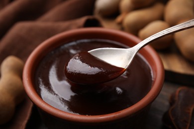 Photo of Taking tasty tamarind sauce with spoon from bowl on table, closeup