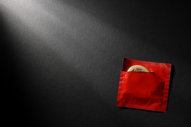 Photo of Condom in torn package on black background, top view with space for text. Safe sex