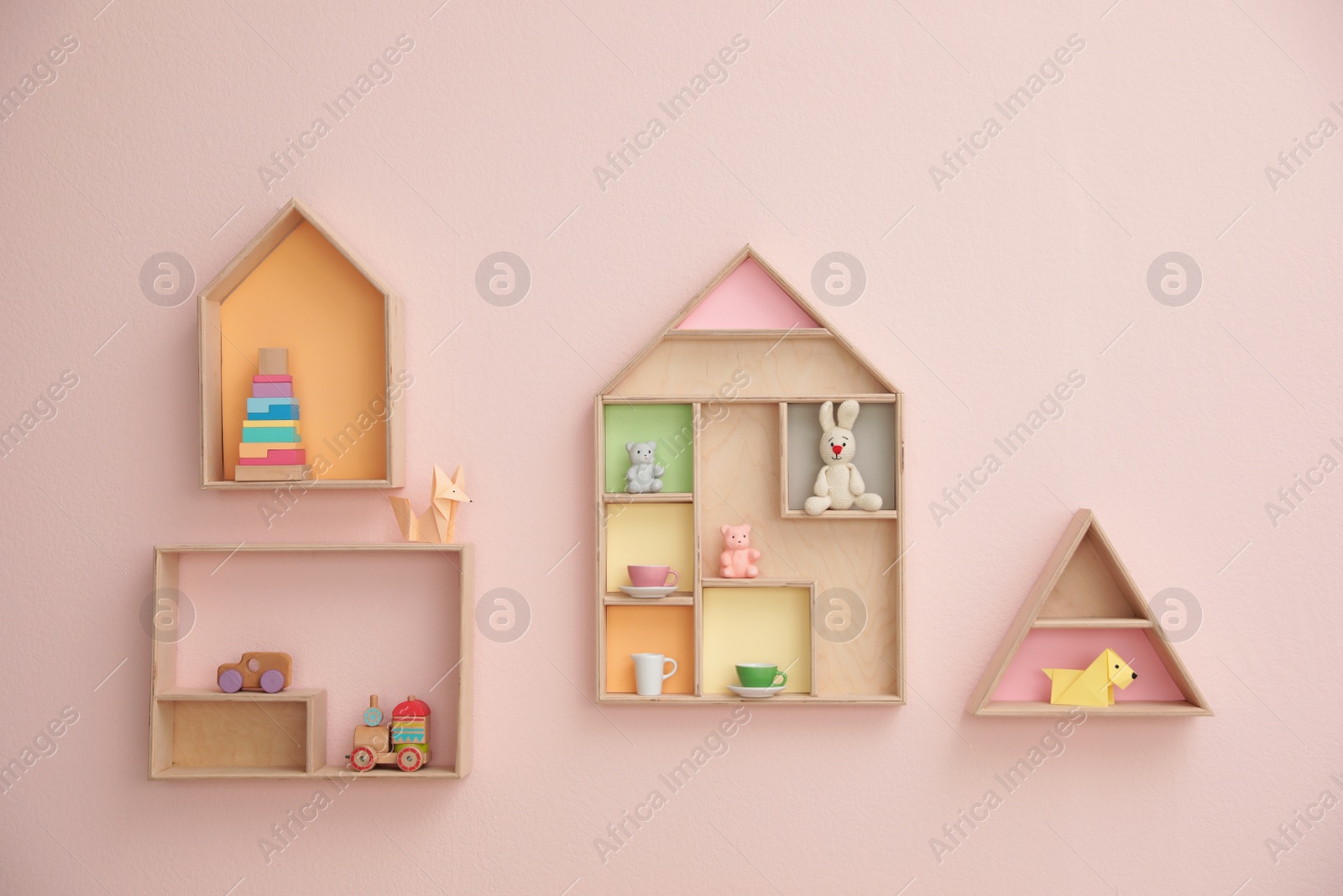 Photo of Stylish house shaped shelves with toys on pink wall. Baby room interior design