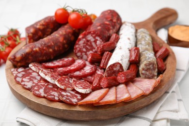 Different types of delicious sausages, sauce and tomatoes served on white tiled table, closeup