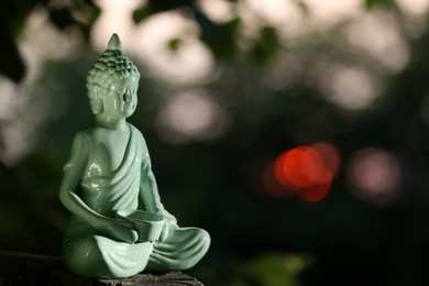 Decorative Buddha statue on stump outdoors in evening, space for text