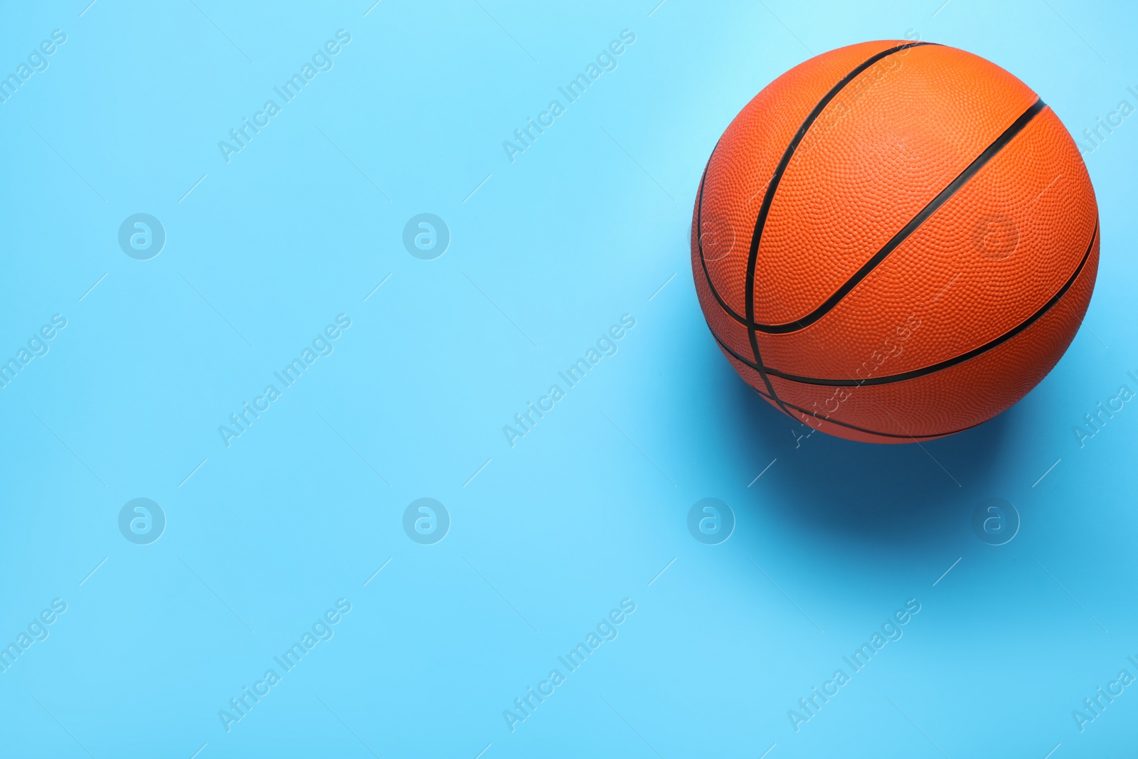 Photo of Orange ball on light blue background, top view with space for text. Basketball equipment