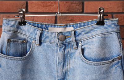 Photo of Hanger with stylish jeans near brick wall, closeup