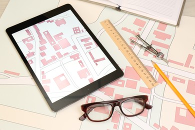 Office stationery, tablet and cadastral maps of territory with buildings on table