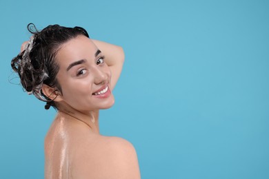 Beautiful happy woman washing hair on light blue background. Space for text