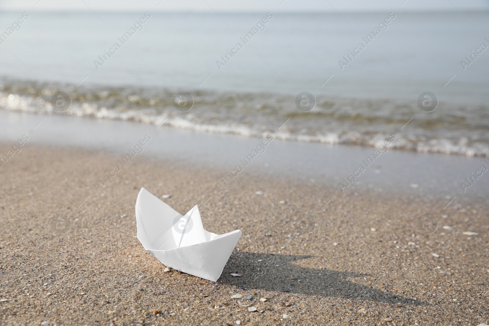 Photo of White paper boat on sandy beach near sea, space for text