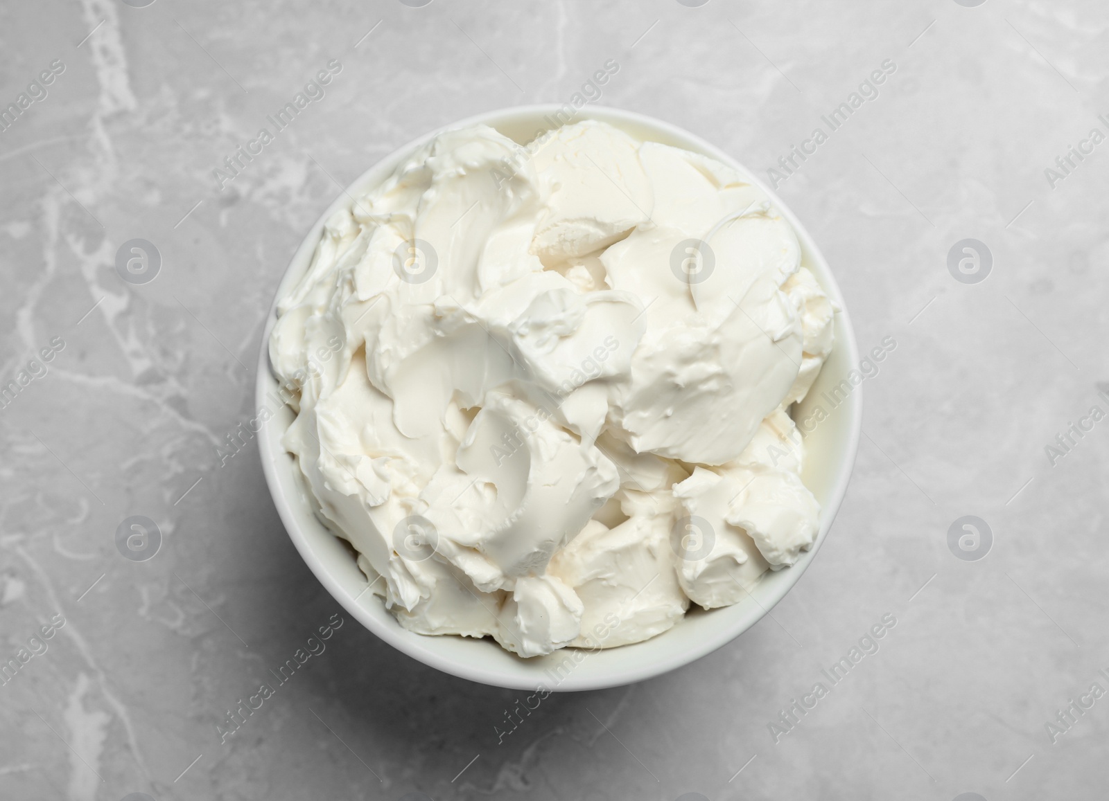 Photo of Bowl of tasty cream cheese on light grey marble table, top view