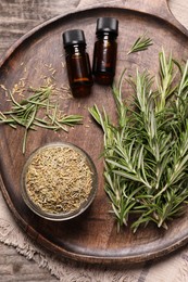 Photo of Bottles of essential oil, fresh and dry rosemary on wooden table, top view