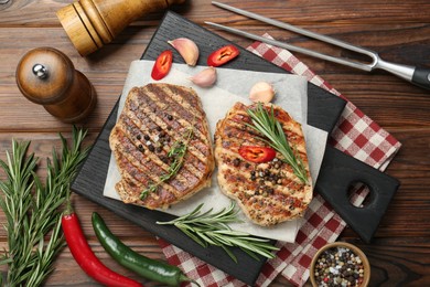 Delicious grilled pork steaks with spices and meat fork on wooden table, flat lay