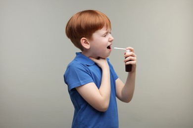 Photo of Little boy using throat spray on grey background