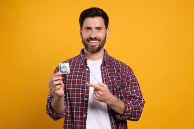 Happy man holding condom on yellow background. Safe sex