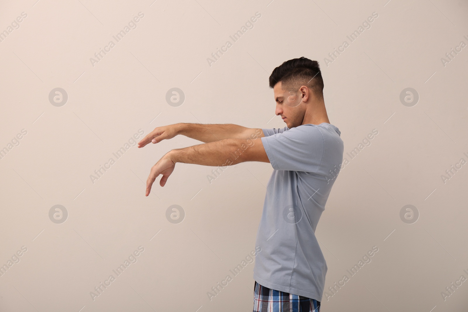 Photo of Somnambulist wearing pajamas on beige background. Sleepwalking