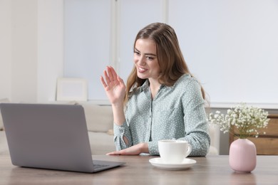 Happy woman having video chat via laptop at wooden table in room