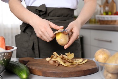 Photo of Woman peeling fresh potato with knife at light table indoors, closeup