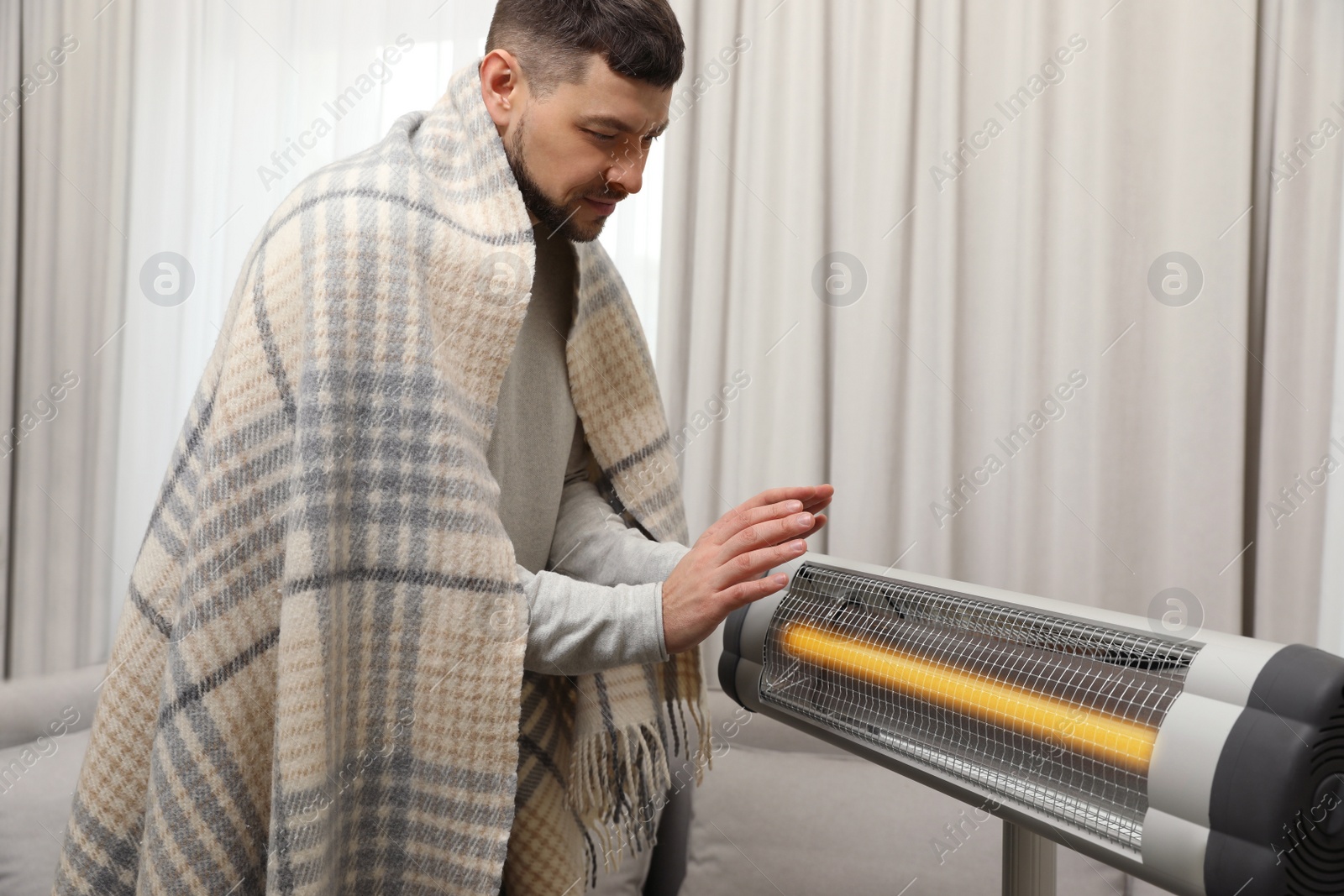 Photo of Man warming hands near electric infrared heater at home