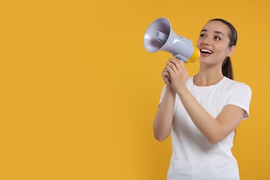 Special promotion. Smiling woman shouting in megaphone on orange background. Space for text