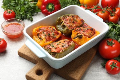 Photo of Tasty stuffed peppers in dish and ingredients on grey table