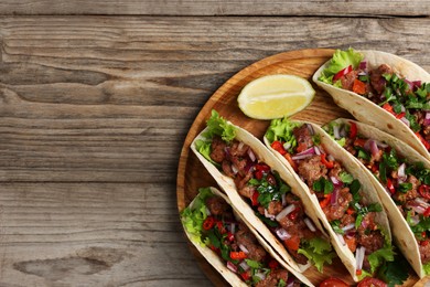 Delicious tacos with meat, vegetables and lime on wooden table, top view. Space for text