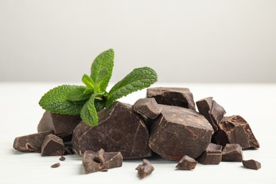 Tasty dark chocolate pieces with mint on white wooden table, closeup
