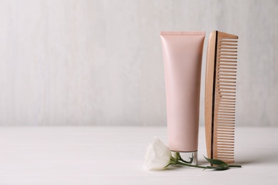 Hair product, flower and comb on white wooden table. Space for text