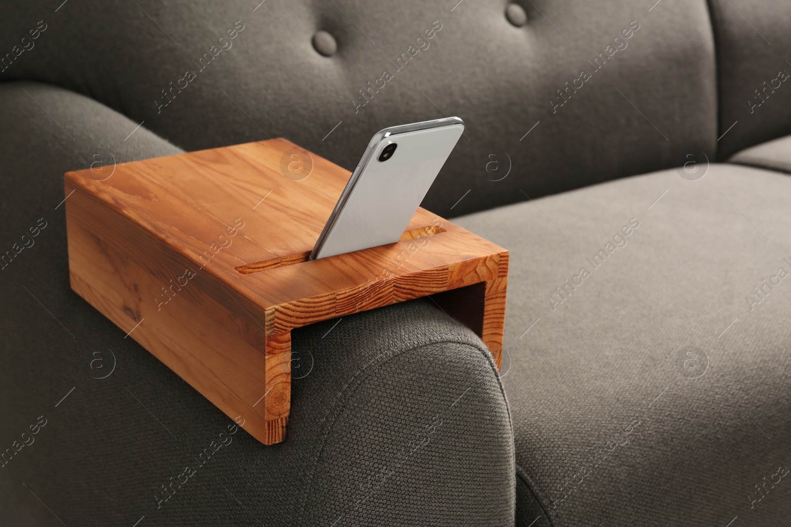 Photo of Smartphone on sofa with wooden armrest table in room, space for text. Interior element