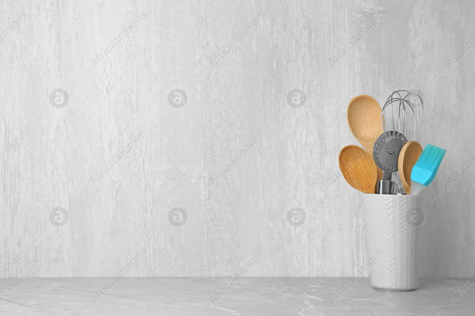 Photo of Holder with kitchen utensils on grey table against light background. Space for text