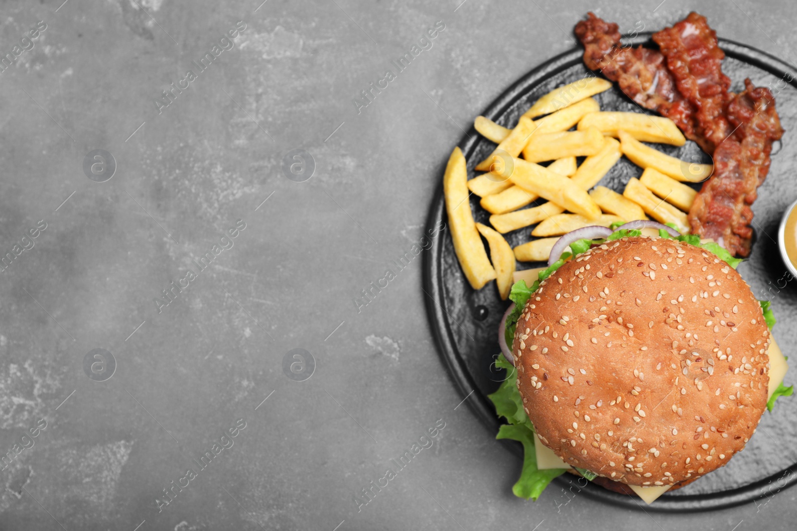 Photo of Frying pan with tasty hamburger and french fries on grey background, top view. Space for text